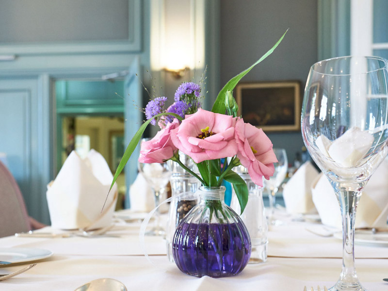 Blumenvase mit bunten Blumen auf Tisch mit weißem Tischtuch