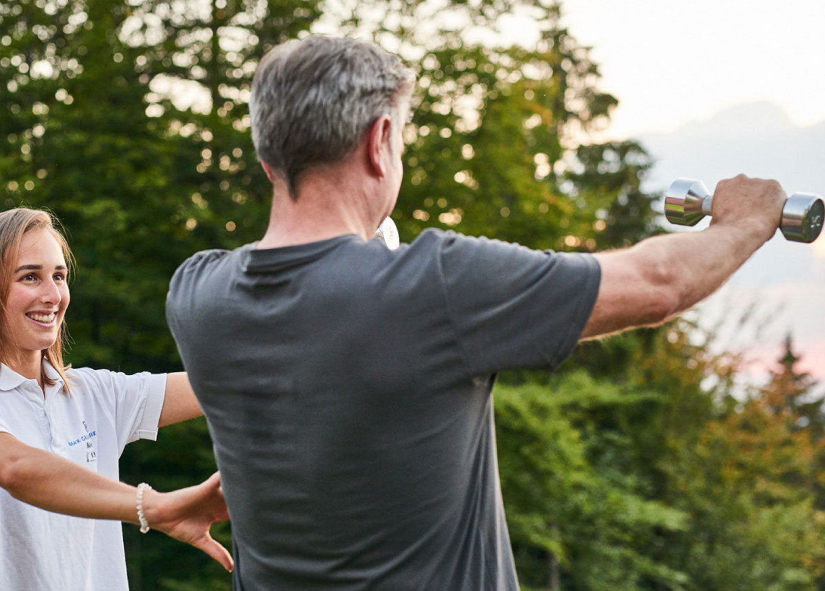 Mann mit Trainerin bei Hantel-Training im Freien